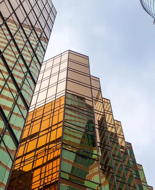 A view from below of modern glass skyscrapers with bright, reflective turquoise panels.