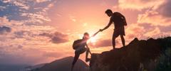 Male and female hikers climbing up mountain cliff and one of them giving helping hand.