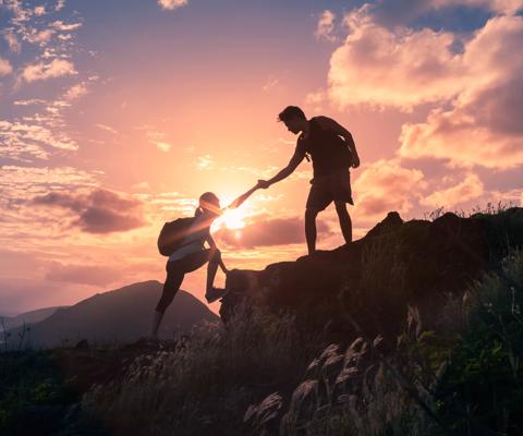 Male and female hikers climbing up mountain cliff and one of them giving helping hand.
