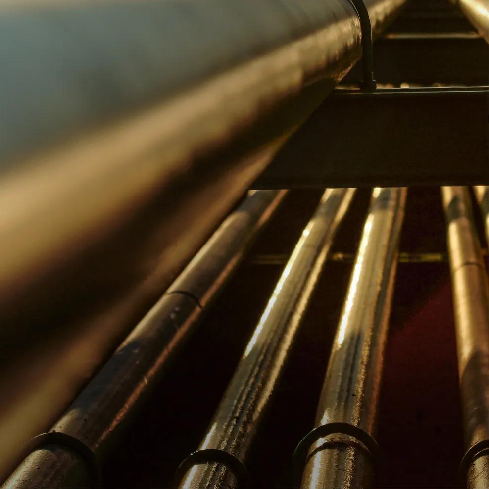 A close-up of a metal pipe with red valves, surrounded by yellow pipes against a clear blue sky.