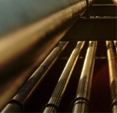 A close-up of a metal pipe with red valves, surrounded by yellow pipes against a clear blue sky.
