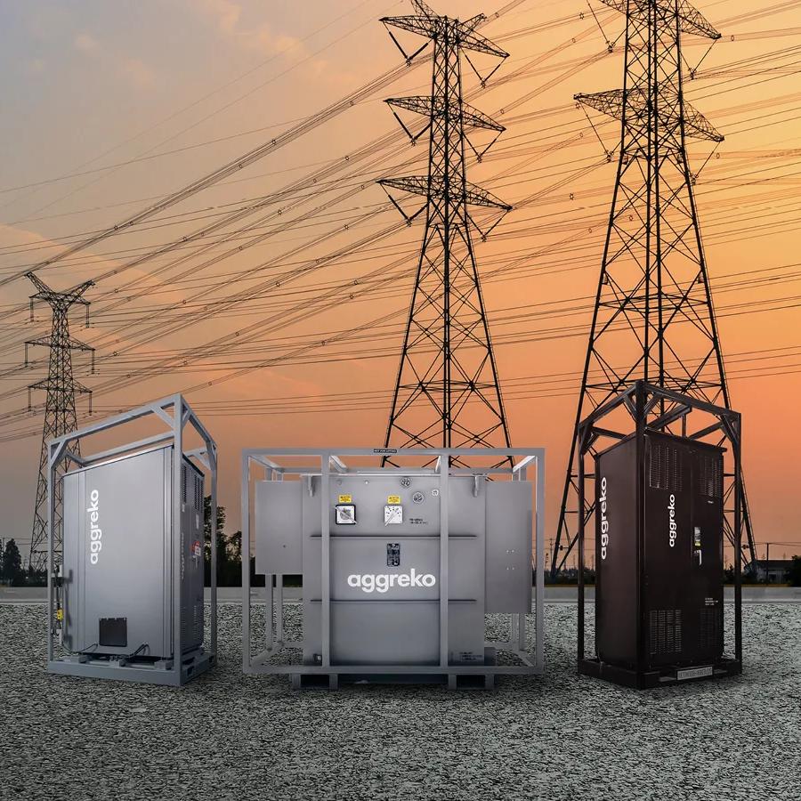 electrical distribution equipment with the Aggreko logo in a gravel floor and power lines behind them