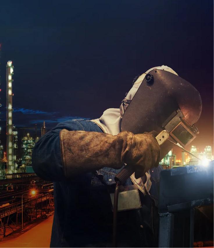 A worker in uniform welding, with a city background at night
