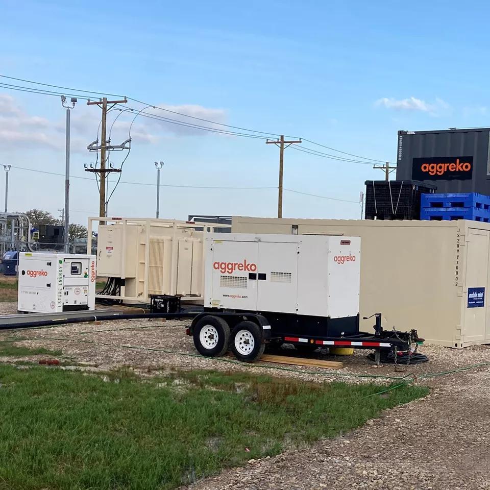 An Aggreko black generator on gravel yard next to another piece of equipment