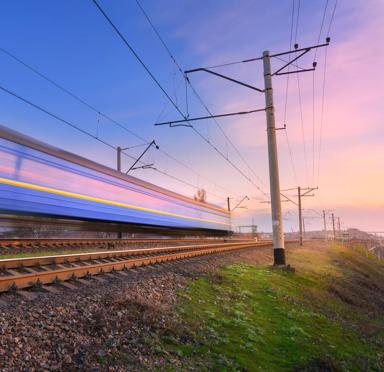 High speed passenger train in motion on railroad at sunset. Blurred commuter train. Railway station against colorful blue sky. Railroad travel, railway tourism. Rural industrial landscape. Concept