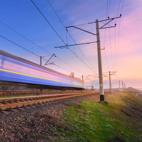 High speed passenger train in motion on railroad at sunset. Blurred commuter train. Railway station against colorful blue sky. Railroad travel, railway tourism. Rural industrial landscape. Concept