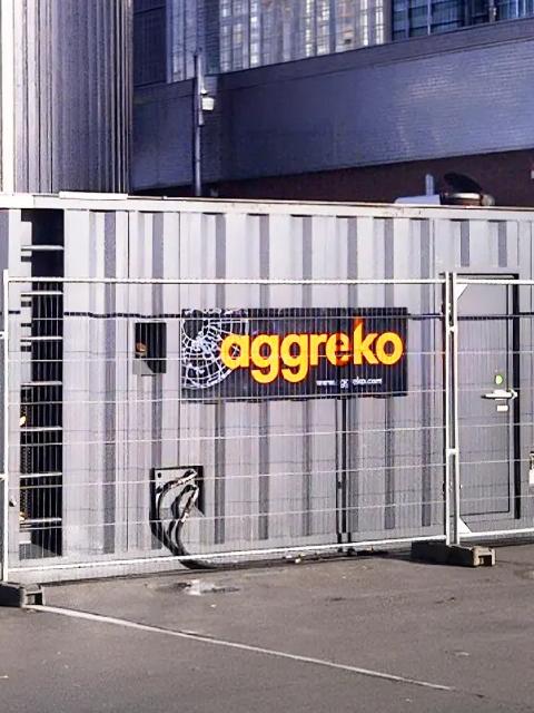 Aggreko industrial equipment enclosed by temporary fencing outside a facility.