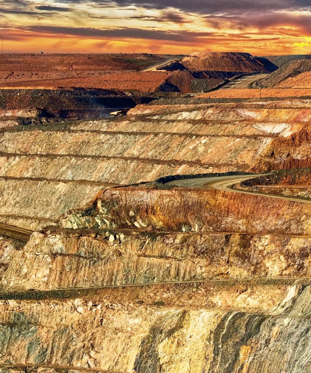 A large, open-pit mine site under a sunset orange and yellow sky.