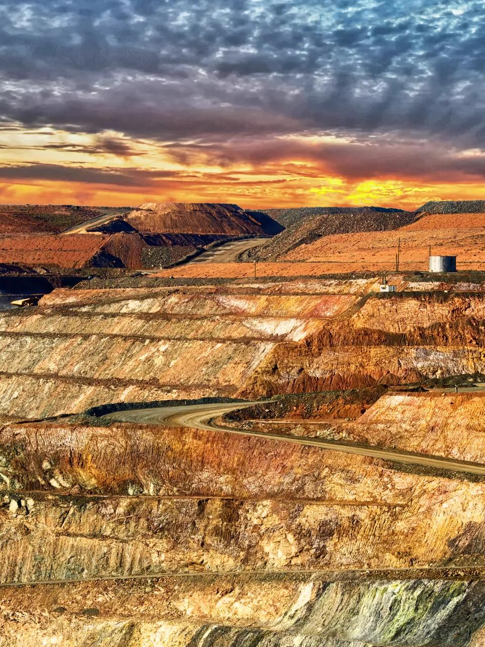A large, open-pit mine site under a sunset orange and yellow sky.