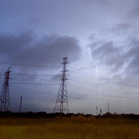 View of a field with transmission towers against a stormy sky and a lightning