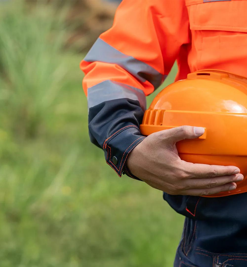 A man wearing an orange safety vest is holding a hard hat