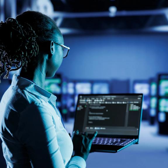 Licensed programmer running code and programming on laptop, troubleshooting and upgrading high tech facility designed to accommodate multiple clusters of fully operational server cabinets