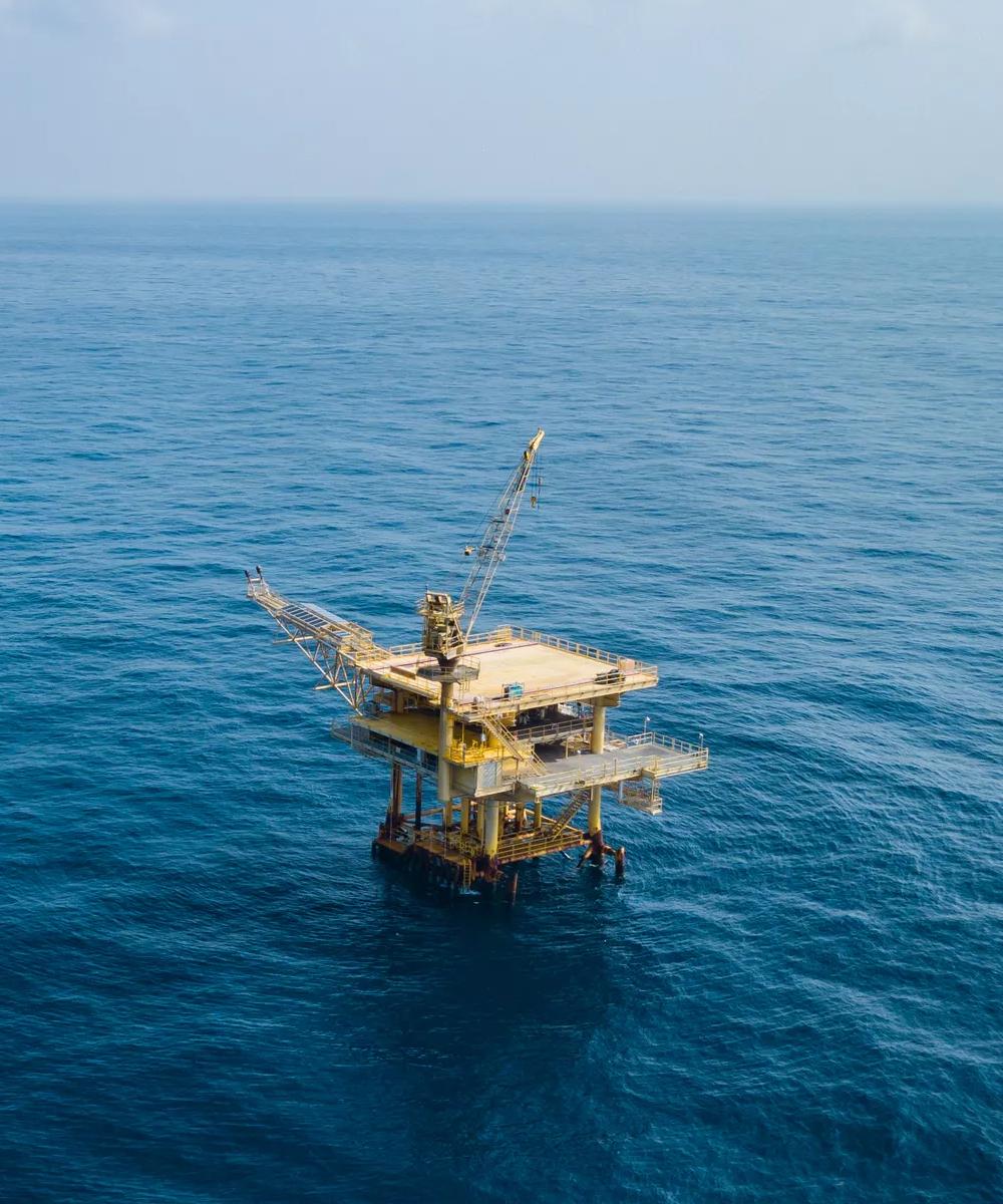 An aerial wide view of a small, fixed offshore oil platform resting in deep blue water.