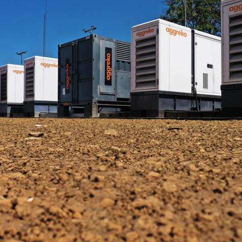 A line of large industrial Aggrekogenerators against a blue sky and a flat, barren landscape.