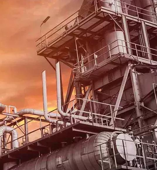 View of the top of a refinery tower against an orange sky.