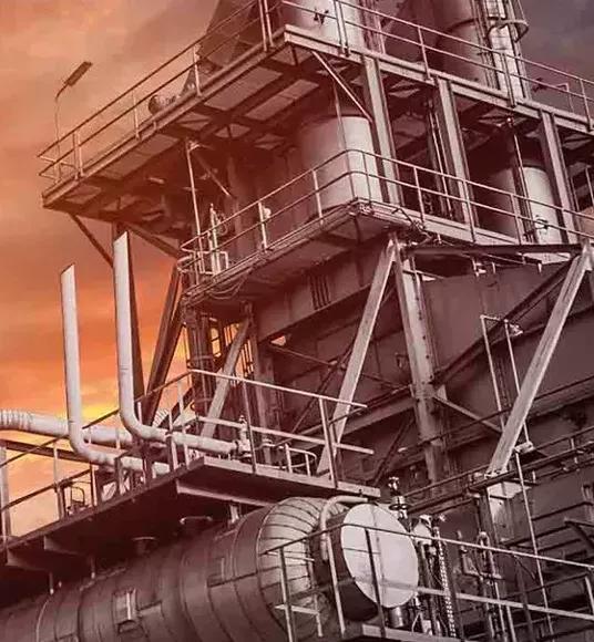 View of the top of a refinery tower against an orange sky.