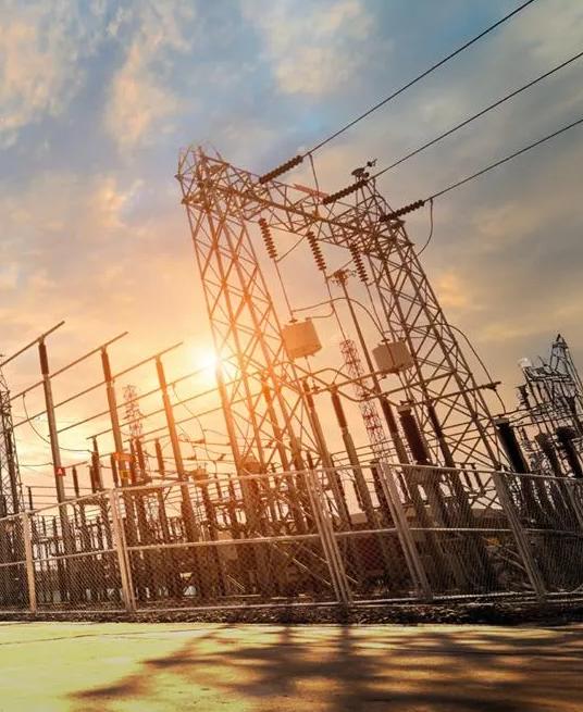 A complex electrical substation with transmission lines and equipment silhouetted against a bright sunset.