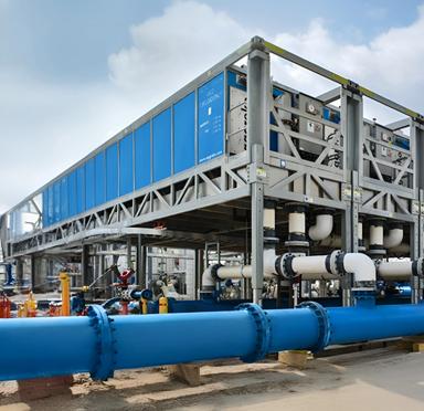 Ground view of a large, blue containerized unit with blue-tinted panels, sitting on an elevated metal support structure outdoors.