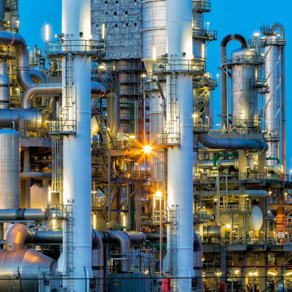 Cut-off view of a refinery's towers under a blue sky.