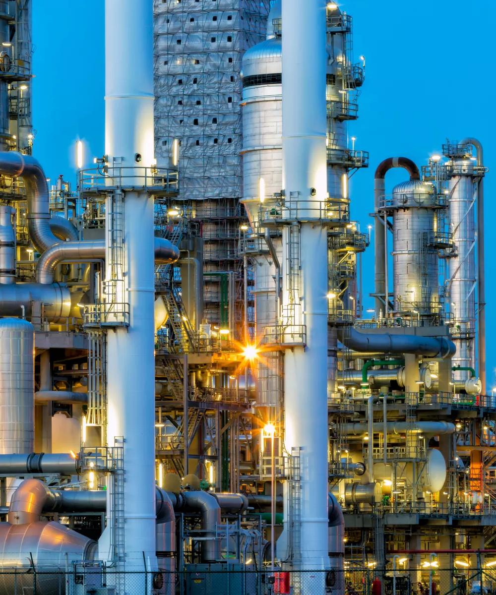 Cut-off view of a refinery's towers under a blue sky.