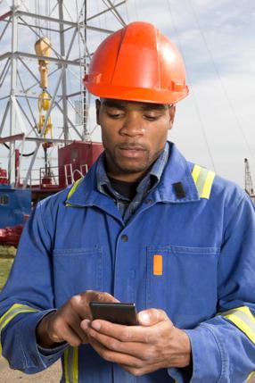 A royalty free image of an oil worker using a smart phone to text while at an oil rig.