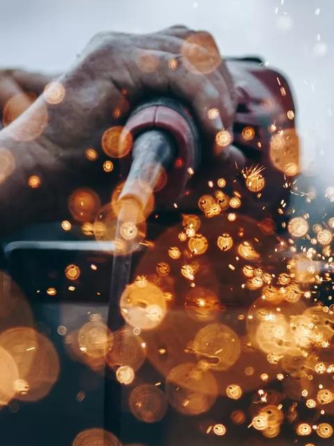 Worker welding metal, creating bright sparks.