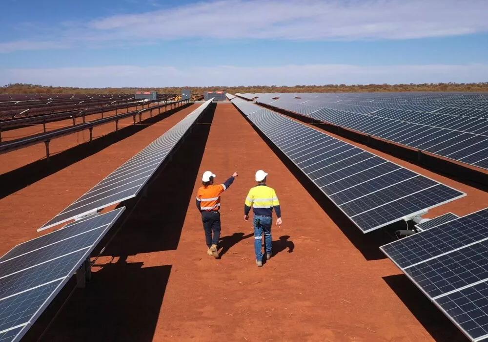 Two workers walking between three rows of solar panel on a red field