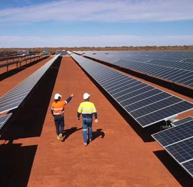 Two workers walking between three rows of solar panel on a red field