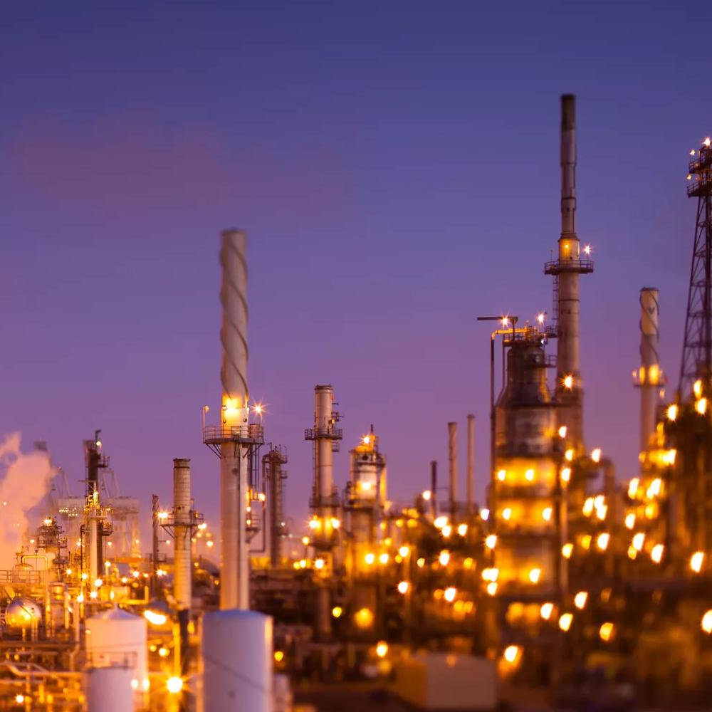 Panoramic view of a lit up refinery at night with a purple sky.
