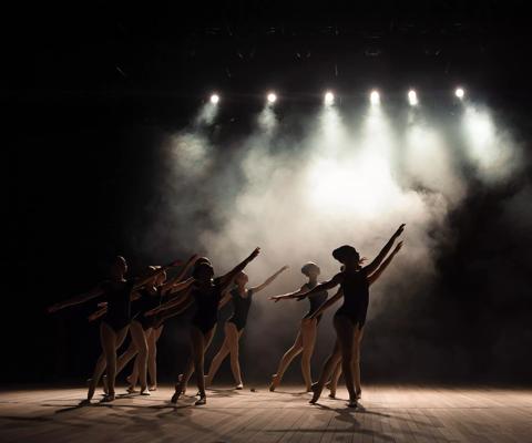 Ballet class on the stage of the theater with light and smoke. Children are engaged in classical exercise on stage.
