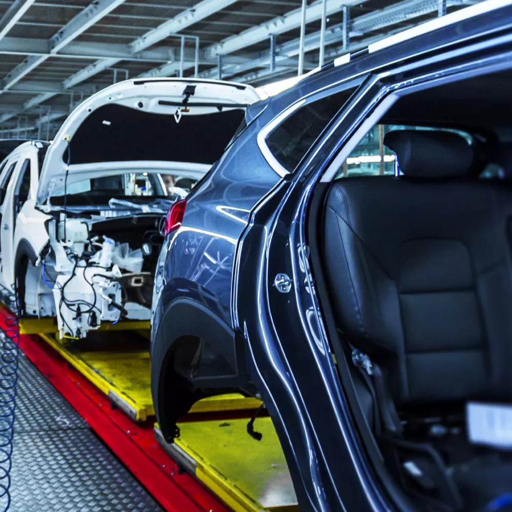 Close-up view of a multiple cars without doors and wheels, and the hoods opened, all moving in an assembly line. 