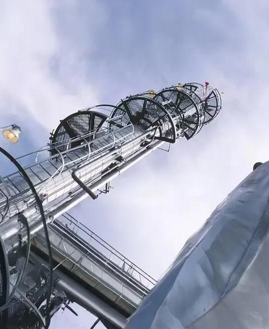 Ground view of a refinery tower under a cloudy sky.