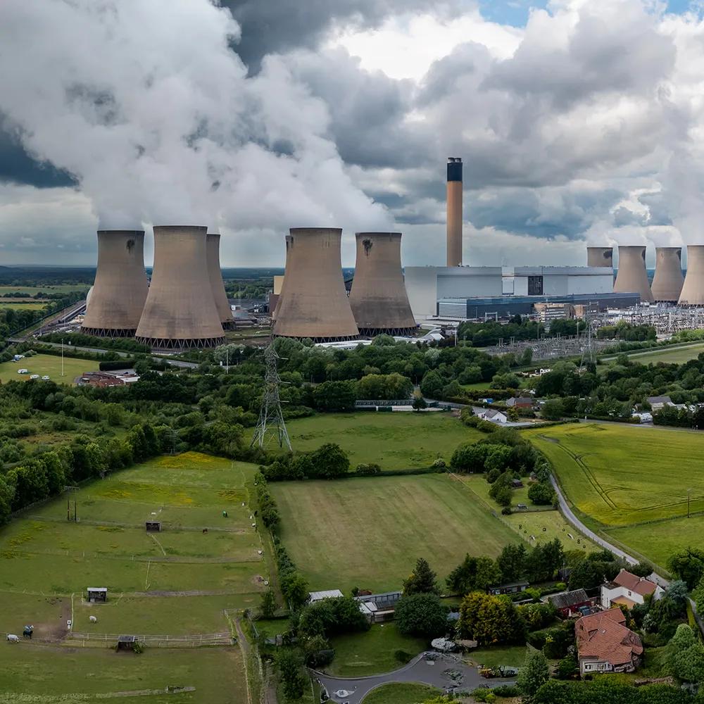 Panoramic view of cooling towers at a nuclear plant in the middle of a green field, under a cloudy sky.