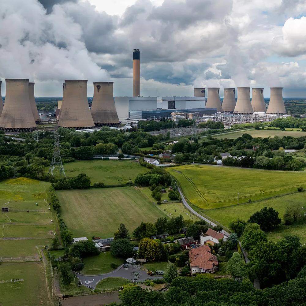 Panoramic view of cooling towers at a nuclear plant in the middle of a green field, under a cloudy sky.