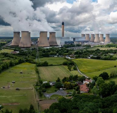 Panoramic view of cooling towers at a nuclear plant in the middle of a green field, under a cloudy sky.