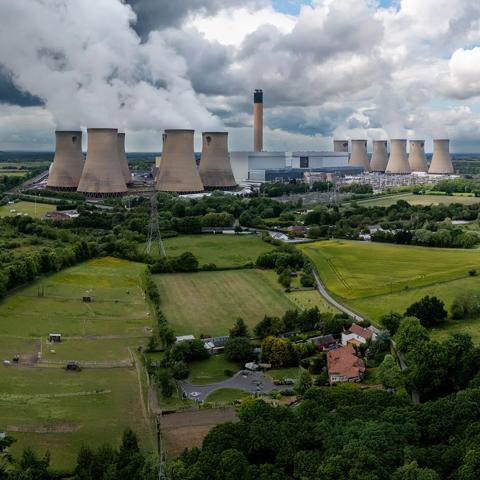 Panoramic view of cooling towers at a nuclear plant in the middle of a green field, under a cloudy sky.