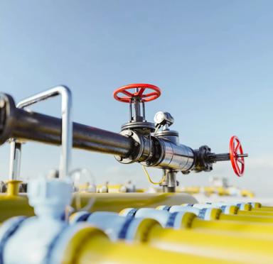 A close-up of a metal pipe with red valves, surrounded by yellow pipes against a clear blue sky.