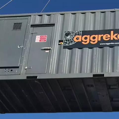 A black Aggreko generator being lifted on a worksite against a blue sky