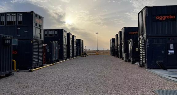  Two rows of Aggreko gas generators in a gravel yard under a cloudy sky