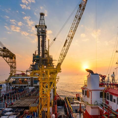 Offshore oil drilling rig operation platform in oil and gas industry with supply boat to transfer chemical during sunrise. Industry concept.