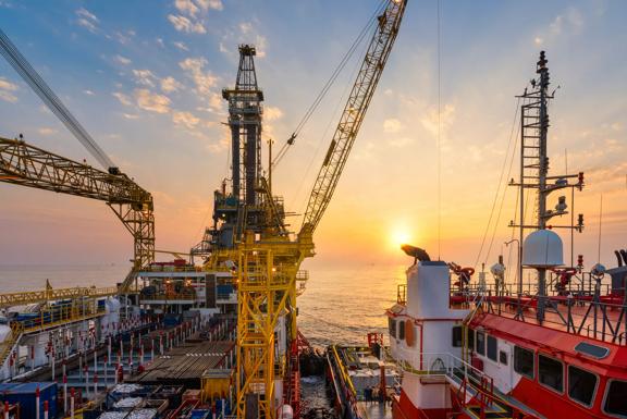 Offshore oil drilling rig operation platform in oil and gas industry with supply boat to transfer chemical during sunrise. Industry concept.