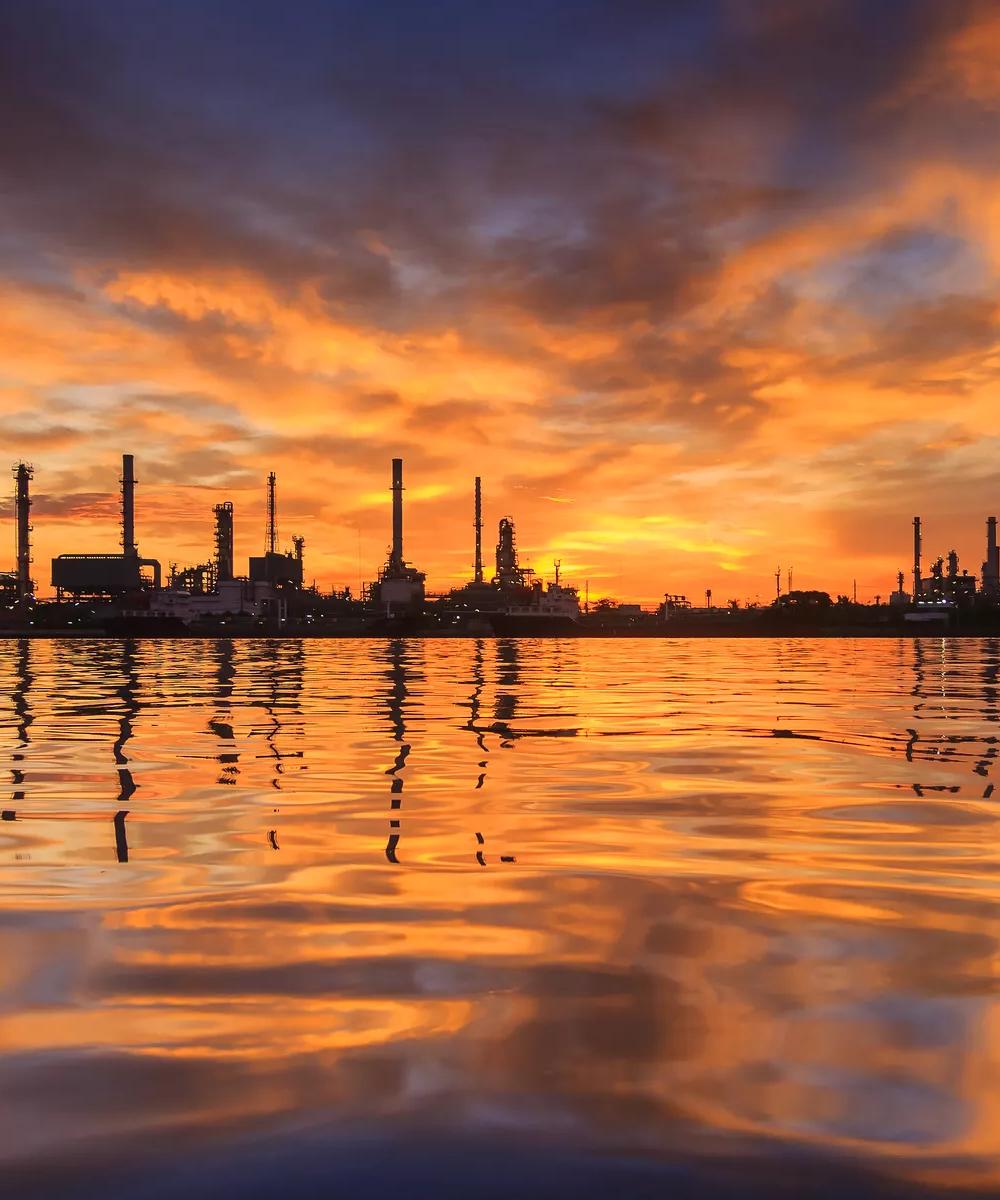 Industrial facility silhouetted against a sunset over the water.