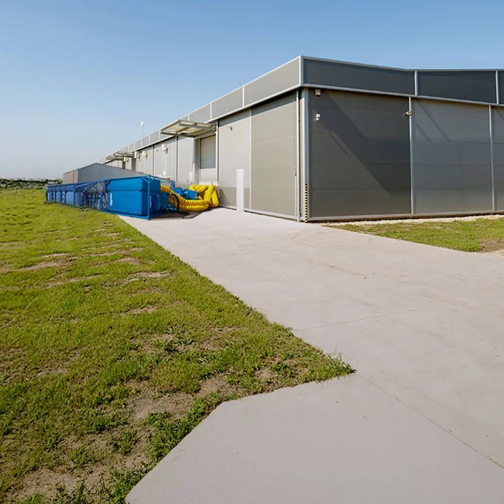 Panoramic view of blue Aggreko cooling equipment outside a building and next to a green field with an electrical plant.