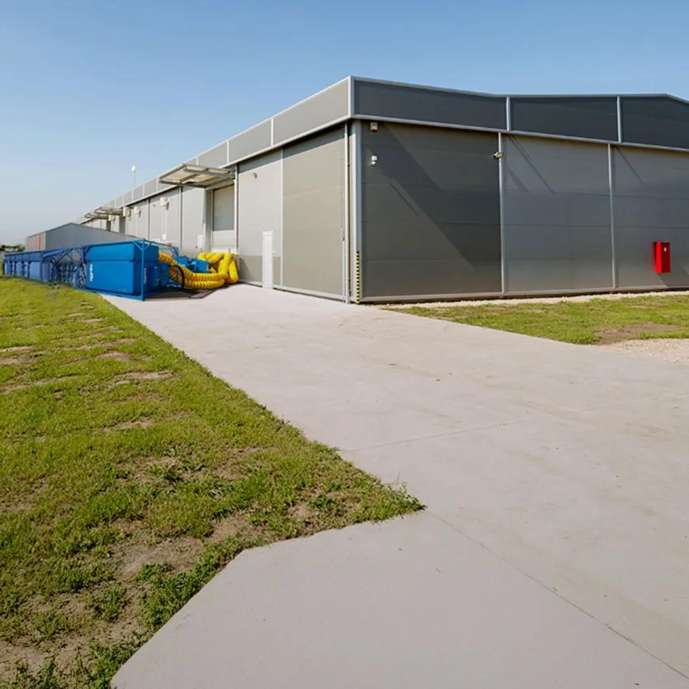 Panoramic view of blue Aggreko cooling equipment outside a building and next to a green field with an electrical plant.