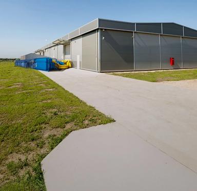 Panoramic view of blue Aggreko cooling equipment outside a building and next to a green field with an electrical plant.