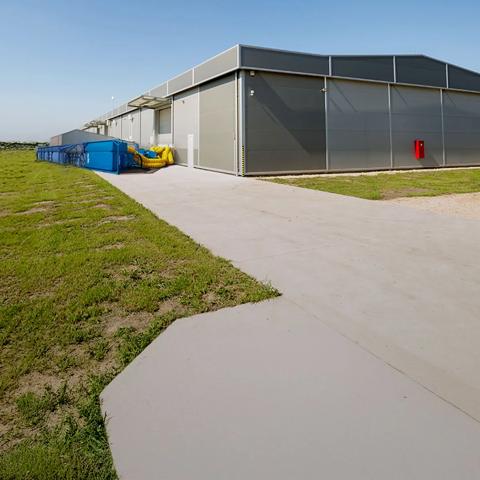 Vue panoramique d’un équipement de refroidissement Aggreko bleu à l’extérieur d’un bâtiment et à côté d’un champ vert avec une centrale électrique.