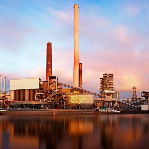 A fossil fuel power plant standing over a lake against a colorful, cloudy sky
