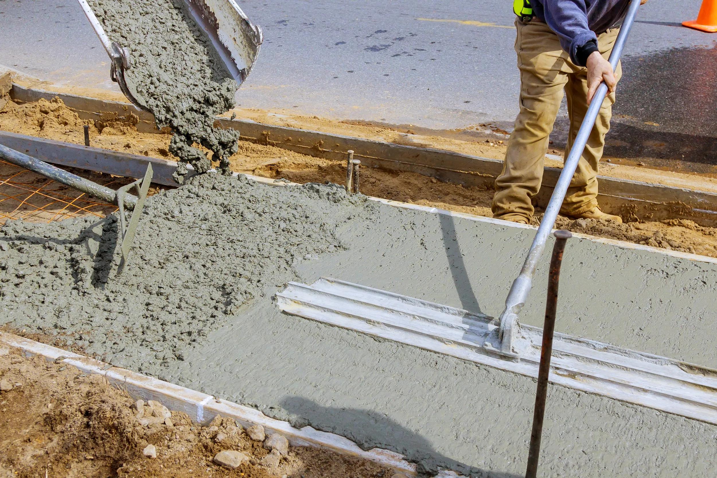 Construction worker pour cement for sidewalk in concrete works with mixer truck with wheelbarrow at construction site filling formwork with cement and gravel