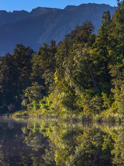 Lac de montagne reflétant des sommets enneigés et la forêt environnante.