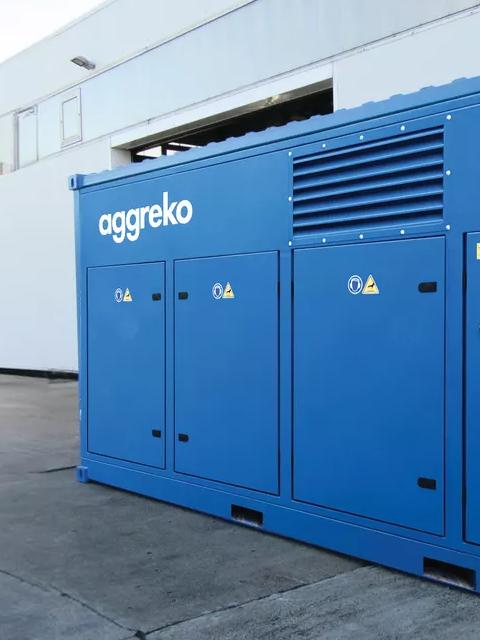 A blue Aggreko electric OFA compressor on the patio between industrial buildings